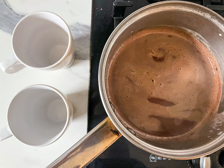 saucepan of hot chocolate and two white mugs