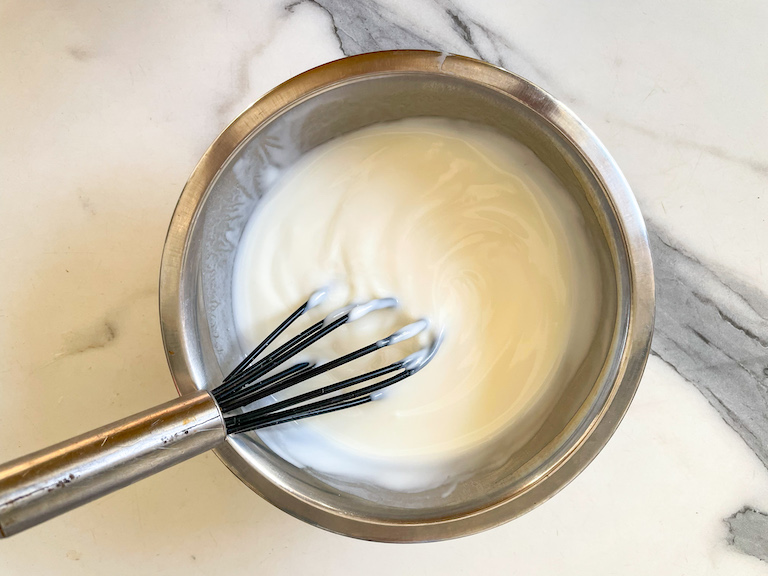 Bowl of plain yogurt with a whisk