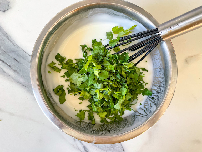 Chopped parsley being added to a bowl of healthy yogurt dip