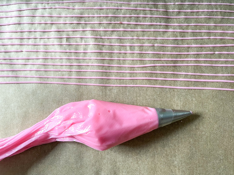 Piping bag of pink icing and rows of piping for homemade sprinkles