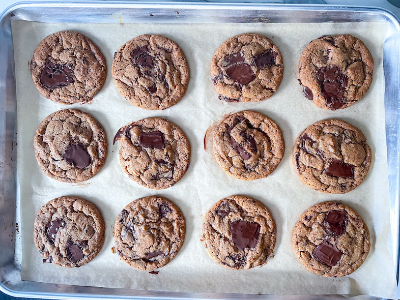 Chocolate tahini cookies on a tray, with large pools of chocolate on top