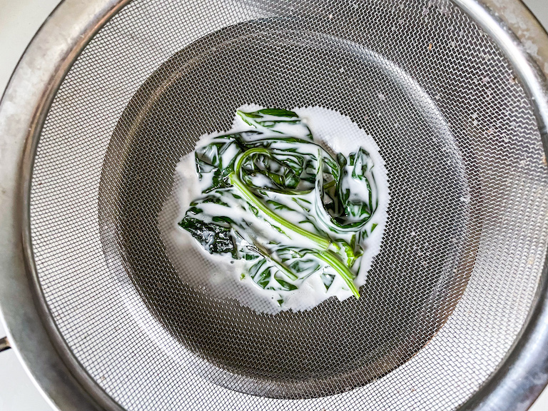A fine mesh strainer with basil leaves covered in coconut cream