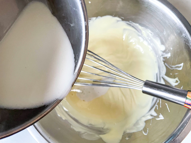 Pouring coconut cream into a bowl of melted white chocolate
