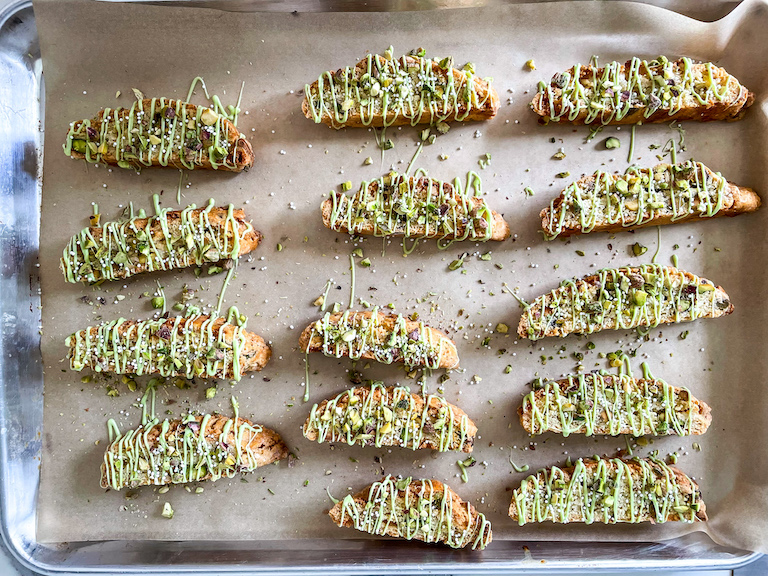 Biscotti slices on a tray, drizzled with white chocolate and sprinkled with pistachios