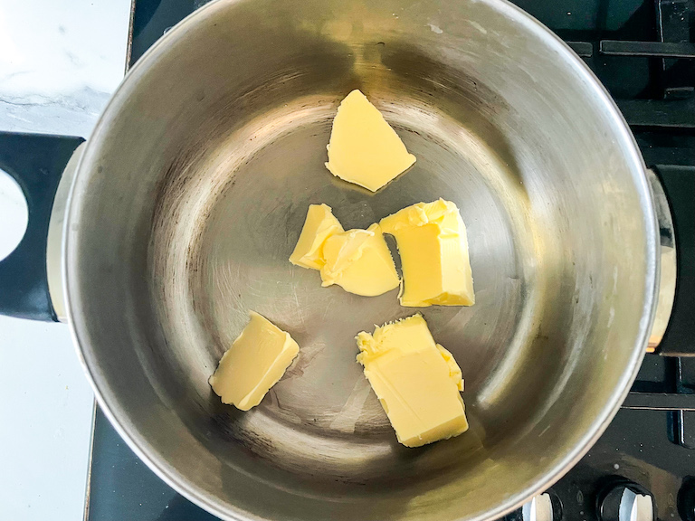A metal pot on a stovetop with chunks of butter
