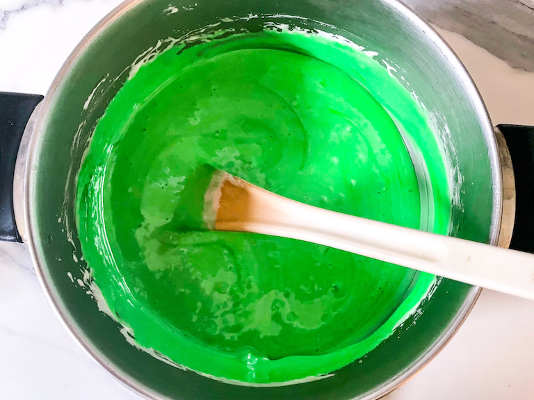 Melting marshmallows and green food coloring in a stock pot to make green rice krispies treats