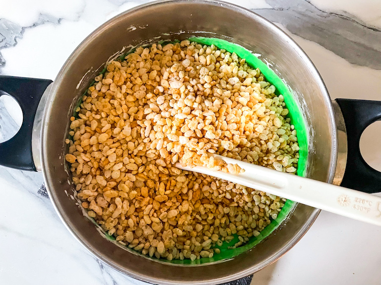 Stirring puffed rice cereal into green marshmallow to make green rice crispy treats