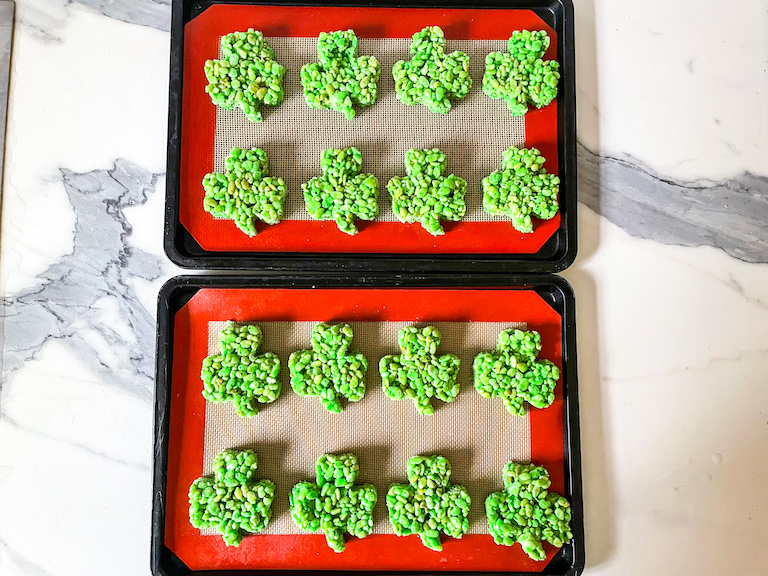 two trays of shamrock rice krispie treats arranged on a marble countertop