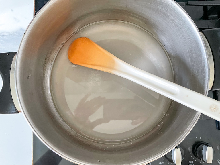 Sugar and glucose syrup in a pot on a stovetop with spoon