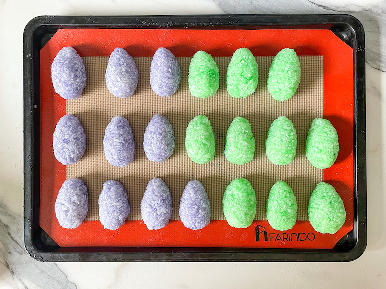 Rows of green and purple coconut Easter eggs arranged on a small tray