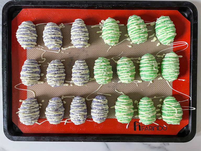 Rows of homemade coconut eggs drizzled in white chocolate, arranged on a silicone mat