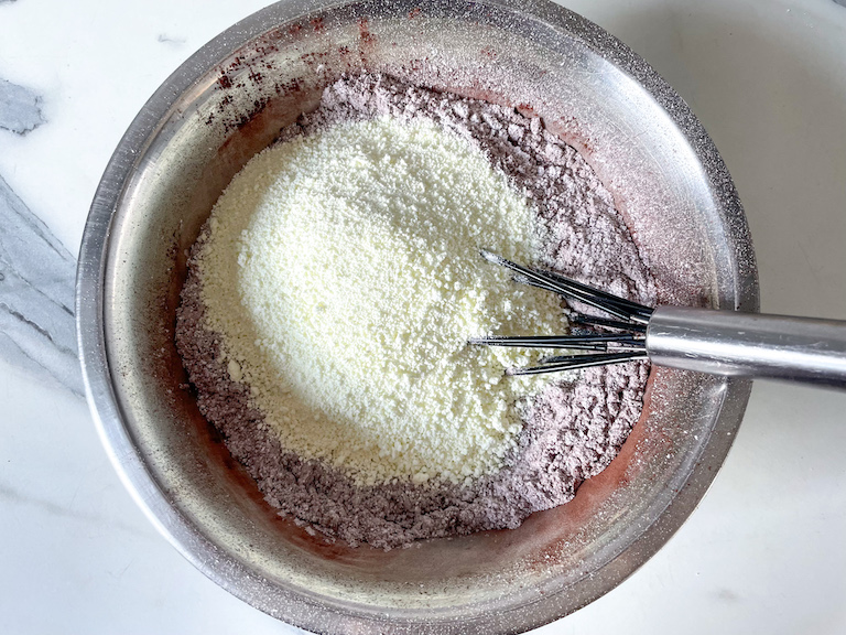 Hot chocolate mix ingredients in a metal bowl with a whisk