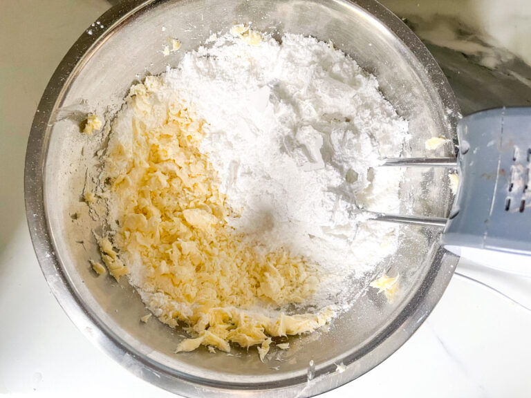 Hand mixer combining butter and confectioner's sugar in a bowl