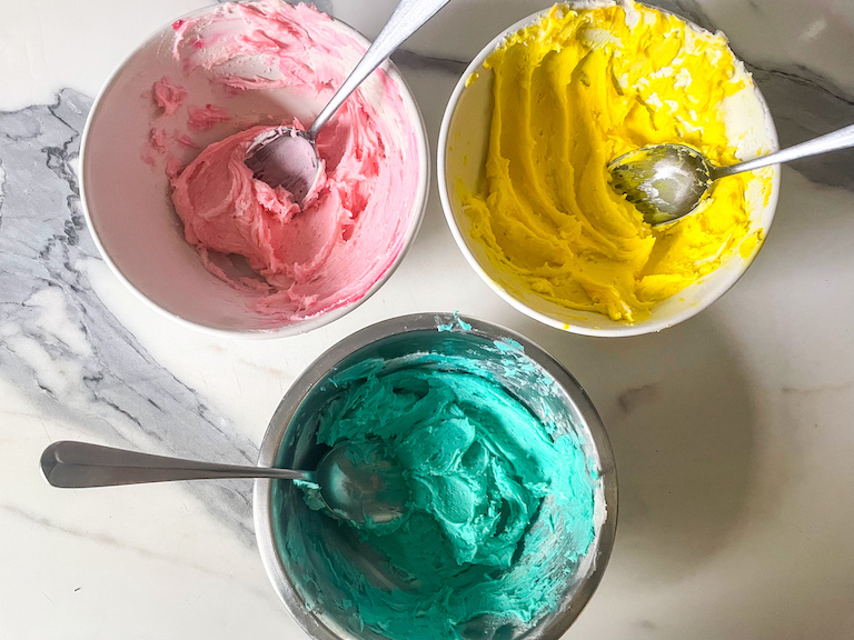 Bowls of pink, yellow, and blue buttercream for decorating brownies for Easter
