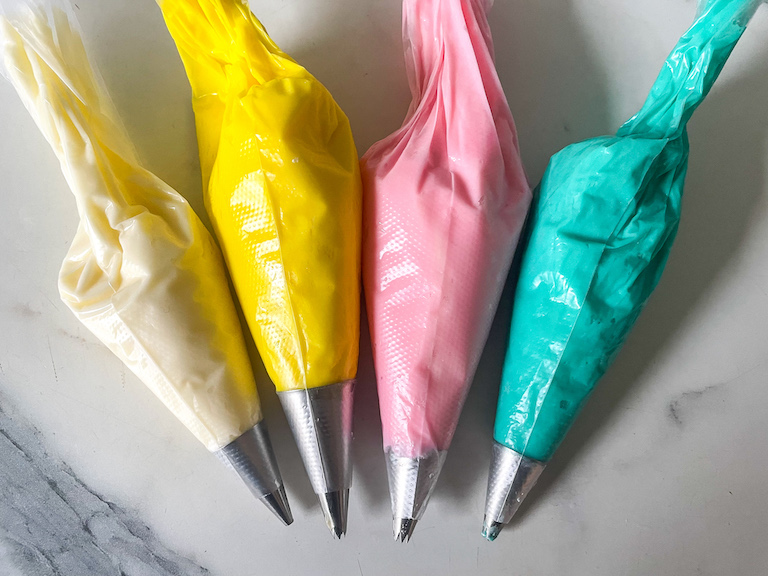 Piping bags with white, yellow, pink, and blue buttercream