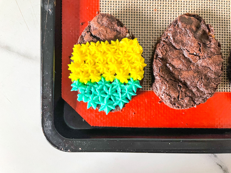Brownie Easter egg with yellow and blue buttercream piping, next to a plain brownie