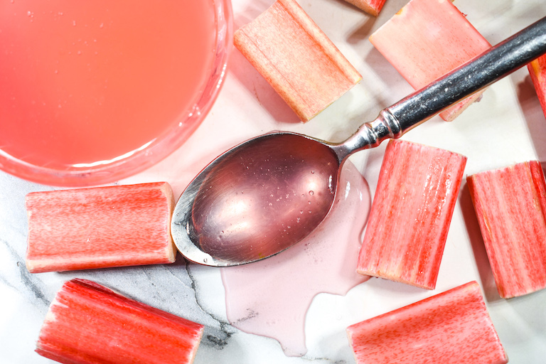 A bowl and spoon of pink rhubarb syrup