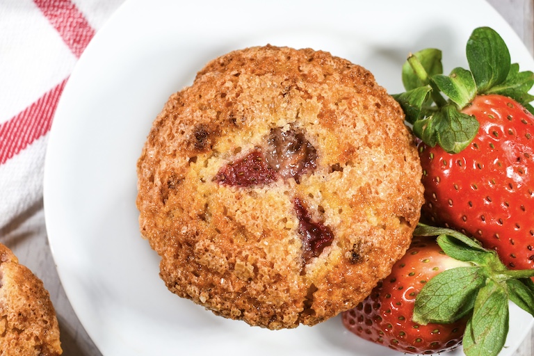 Close up shot of a strawberry muffin on a plate with two berries