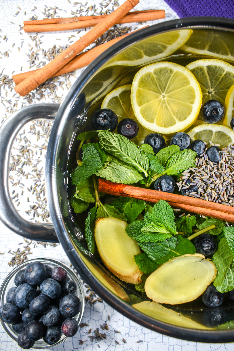 Vertical photo of a spring simmer pot, with cinnamon sticks and bowl of blueberries