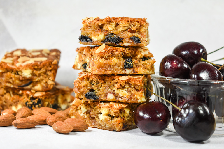 A stack of blonde brownies, almonds, and fresh cherries