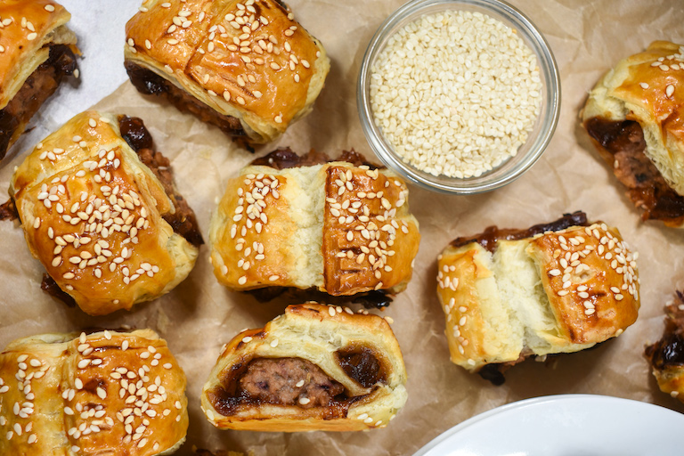 Meatless sausage rolls arranged on parchment with a dish of sesame seeds