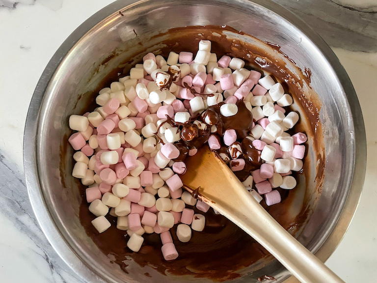 Pink and white marshmallows in a bowl of chocolate with a spoon