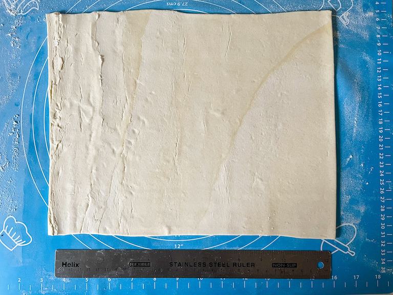 Sheet of puff pastry and a ruler on a blue rolling mat