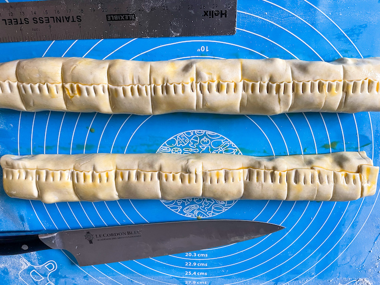 Two rolls of puff pastry and a knife on a blue rolling mat