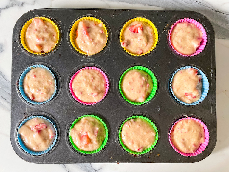 Strawberry muffin batter portioned into silicone cups in a muffin tin