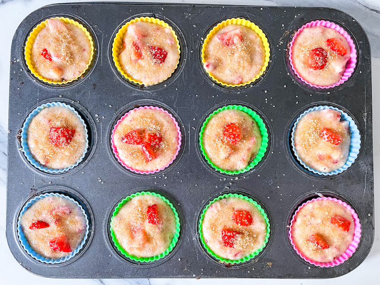 Demerara sugar sprinkled on top of cups of strawberry muffin batter