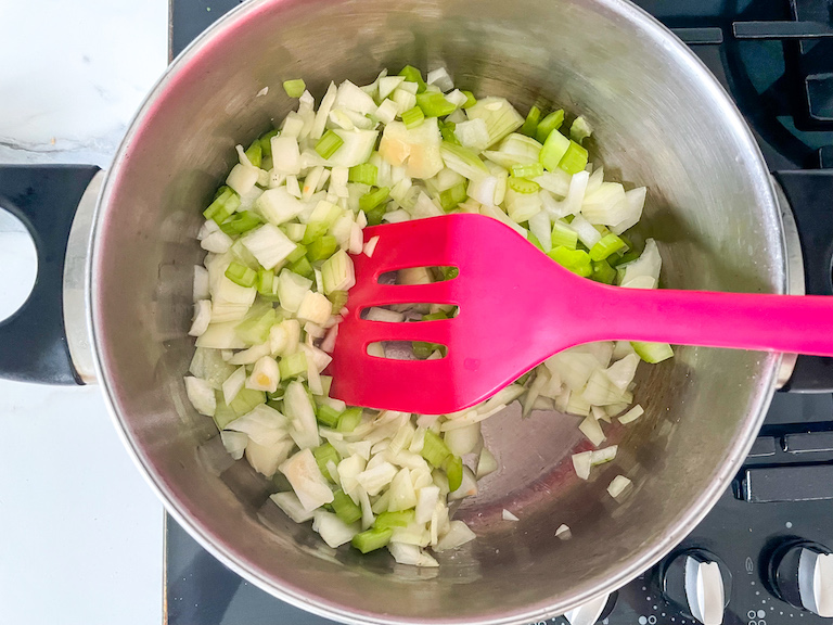 A spatula stirring onions and celery in a stock pot