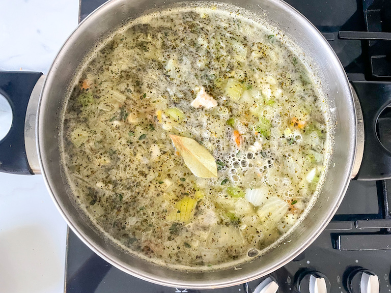 A pot of vegetarian chicken noodle soup on the stove top with a bay leaf floating on top