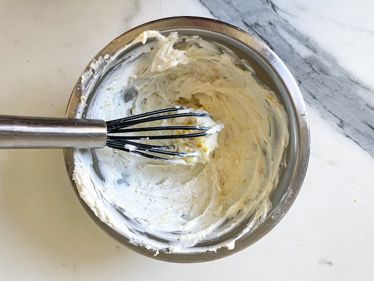 A whisk with goat cheese and lemon zest in a bowl