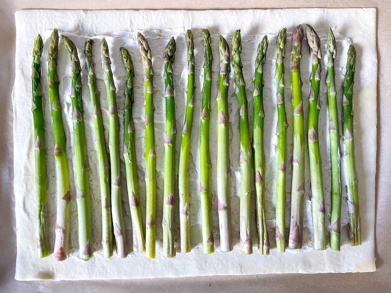 A row of asparagus spears on a sheet of puff pastry