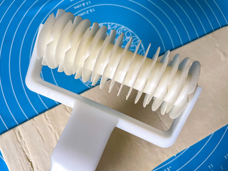 A white plastic lattice cutter and a strip of puff pastry on a silicone mat
