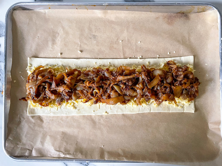 Caramelized onions arranged on top of cheese, on a rectangle of puff pastry