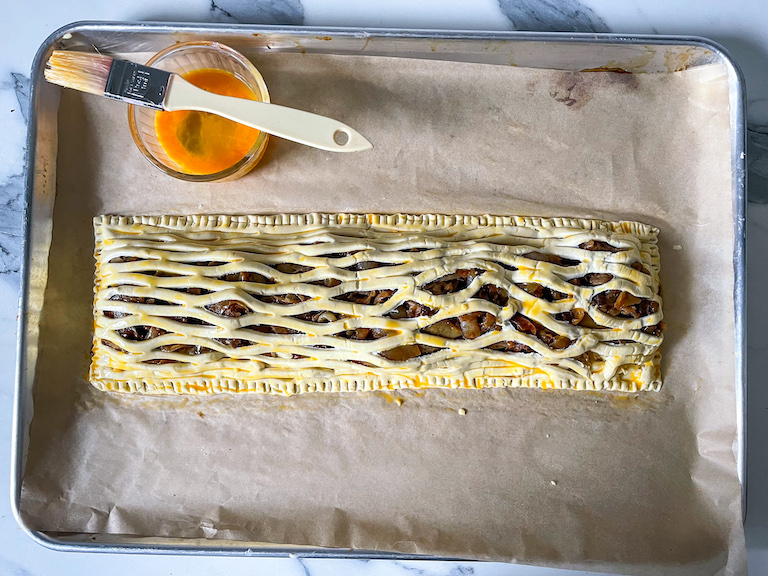 Lattice pastry on a tray with a dish of egg wash and a pastry brush