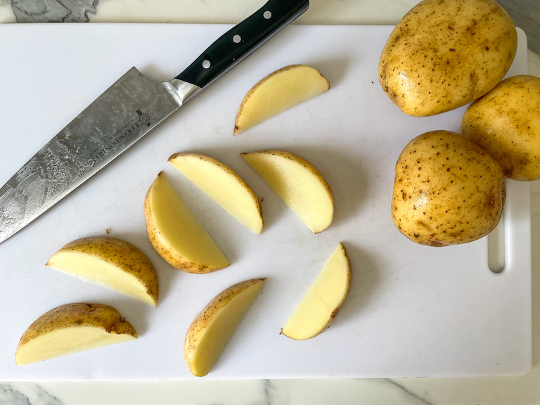 Potato wedges and a chef's knife on a cutting board