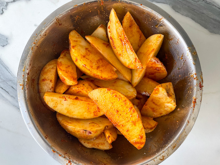 A bowl of potato wedges coated in spices and oil