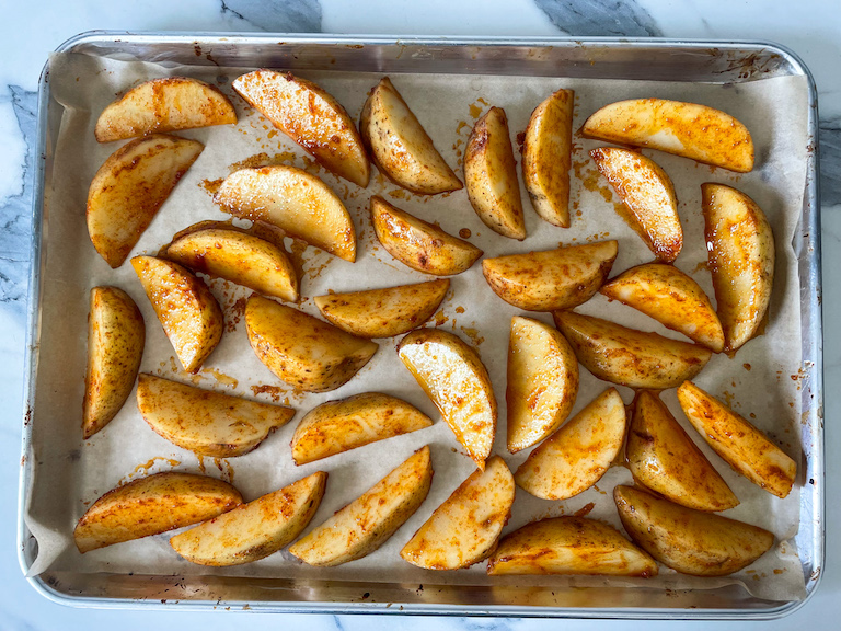 Potato wedges covered in oil and spices, on a tray