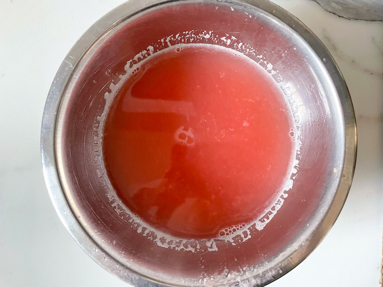 Pink rhubarb water strained into a bowl