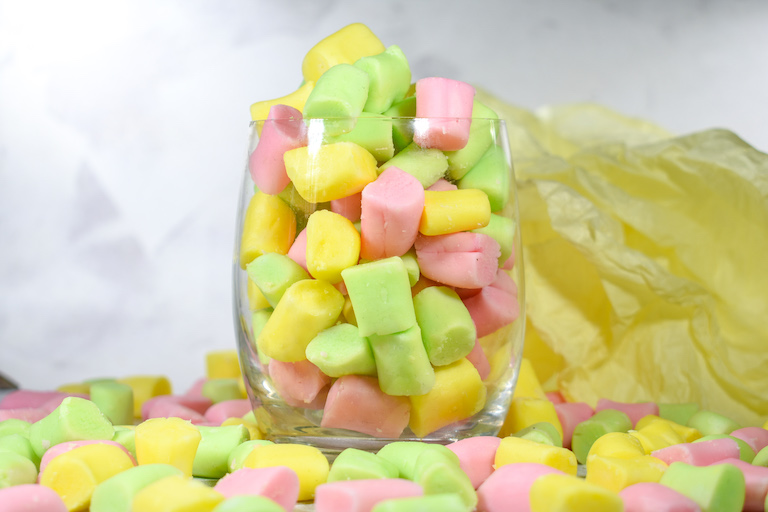 A glass of pastel colored butter mints, with a sheet of yellow tissue paper in the background