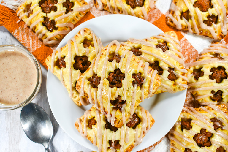Pumpkin hand pies arranged on a white plate, with a checkered orange towel and dish of brown sugar frosting