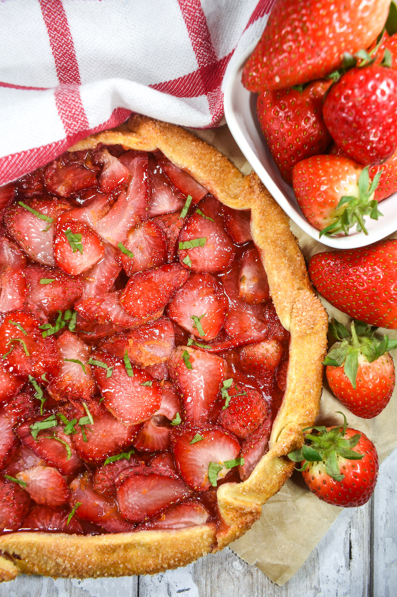 strawberry galette, fresh berries, and tea towel arranged on a sheet of parchment