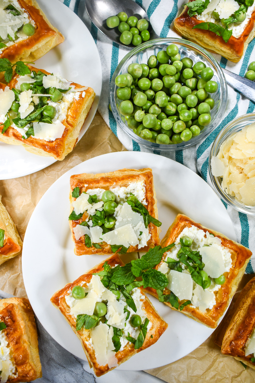 A bowl of peas and two plates with puff pastry and ricotta tarts