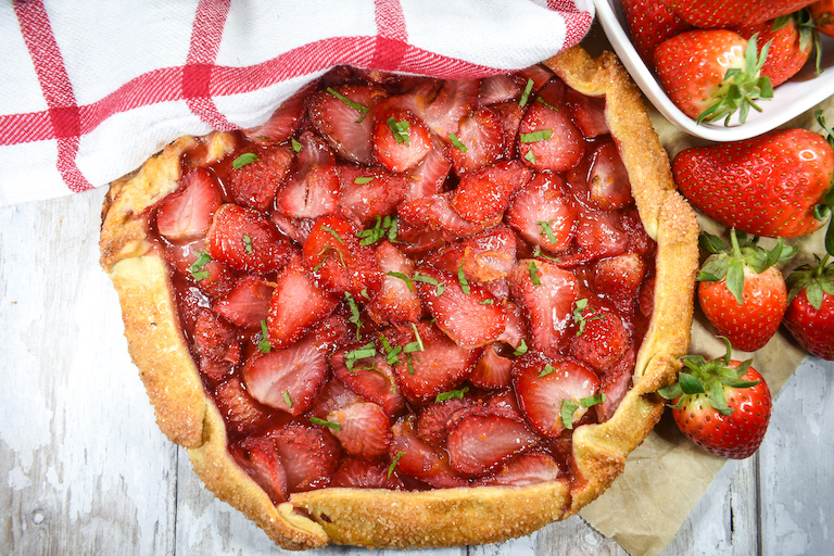 Berry galette on a wooden surface with tea towel and red strawberries