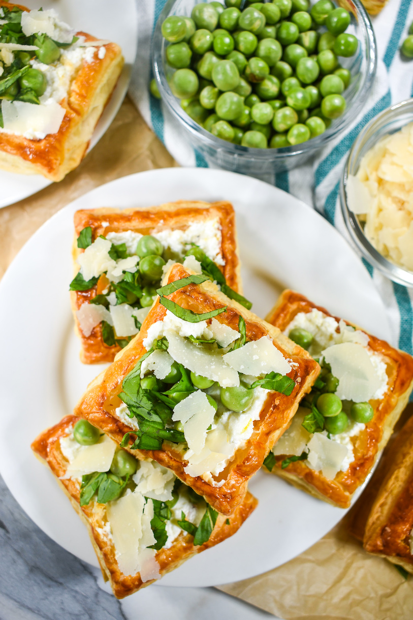 Puff pastry with ricotta and peas, arranged on a white plate with a bowl of peas and bowl of Parmesan cheese