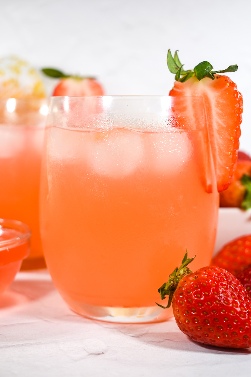 A glass of rhubarb and strawberry lemonade with a slice of fresh strawberry