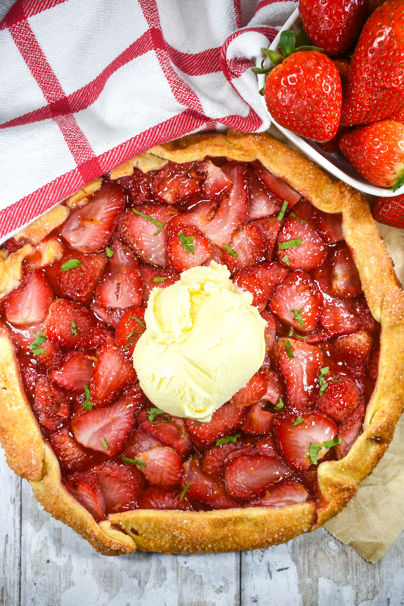 Looking down at a strawberry galette topped with a scoop of vanilla ice cream