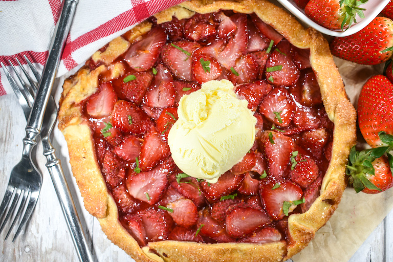 Strawberry galette with a dish of berries, forks, tea towel, and scoop of ice cream